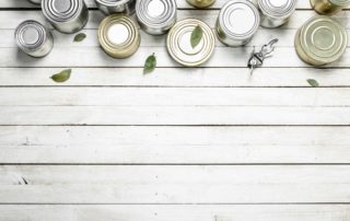 Canned food and a can opener arranged on a wooden surface.