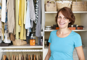 A smiling woman standing in front of an organized closet filled with clothes and accessories.