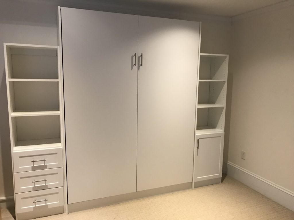 A white closet with built-in shelves and drawers in a room with beige carpeting.