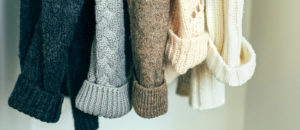 A row of knitted sweaters hanging in natural light.