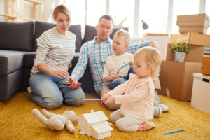Family organization spending time together in a new home, with parents watching their children play on the floor.