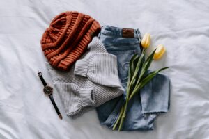 Casual outfit organized with jeans, a sweater and beanie, accessorized with a watch and tulips on a bed.