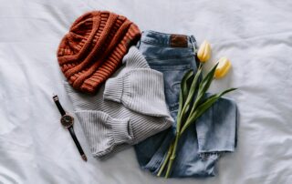 Casual outfit organized with jeans, a sweater and beanie, accessorized with a watch and tulips on a bed.