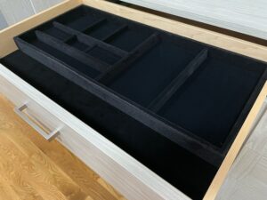 Open wooden closet drawer with black felt-lined organizers inside.