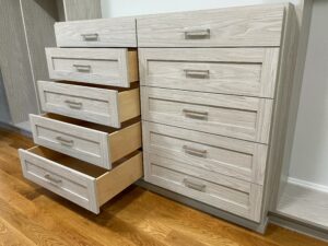 A light wooden closet dresser with multiple open drawers.