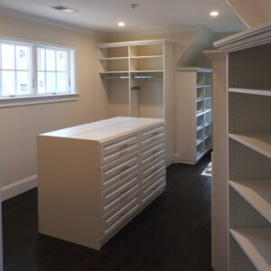 A spacious walk-in closet with empty shelves and a central island with drawers.