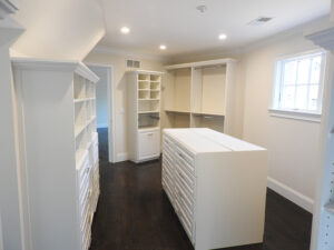 A spacious walk-in closet with white cabinetry and dark hardwood floors.