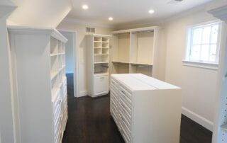 A spacious walk-in closet with white cabinetry and dark hardwood floors.