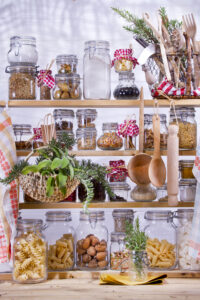 An organized pantry shelf with various jars containing dry food items and kitchen utensils.