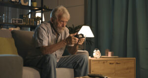 Elderly man with a remote control watching television with intense focus in his dimly lit man cave.