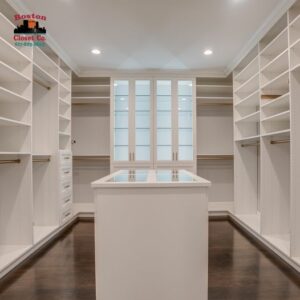 An empty walk-in closet with white shelving units and a central island, designed for optimal closet organization, featuring a window for natural light.