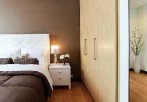 Modern bedroom interior featuring a white bed with a tufted headboard, brown bedding fresh from spring cleaning, a white nightstand with a lamp, and a large mirror.