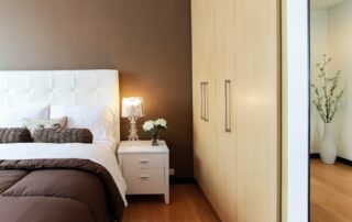 Modern bedroom interior featuring a white bed with a tufted headboard, brown bedding fresh from spring cleaning, a white nightstand with a lamp, and a large mirror.