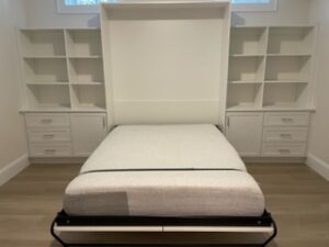 A Murphy bed in the lowered position with surrounding built-in shelves and drawers in a clean room.
