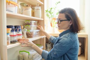 Woman organizing pantry shelves with various food containers in the pantry.
