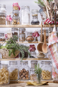 Organized pantry shelves stocked with various dry food in glass jars and kitchen utensils.
