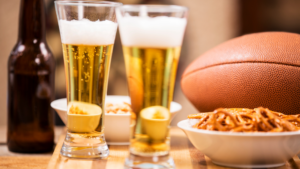 Two glasses of beer with snacks and a football on a wooden table in a man cave.