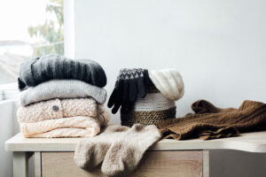 Organized winter clothes and accessories arranged on a wooden dresser near a window.