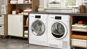 Modern laundry room with a washer and dryer under a countertop, flanked by storage shelves with linens and baskets.