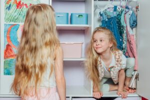 Young kid crouching inside a closet, playfully peeking out at another girl.