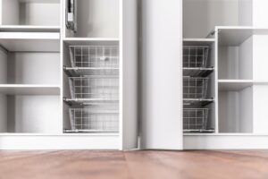 Empty white shelves with two pull-out wire baskets in an open reach-in closet.