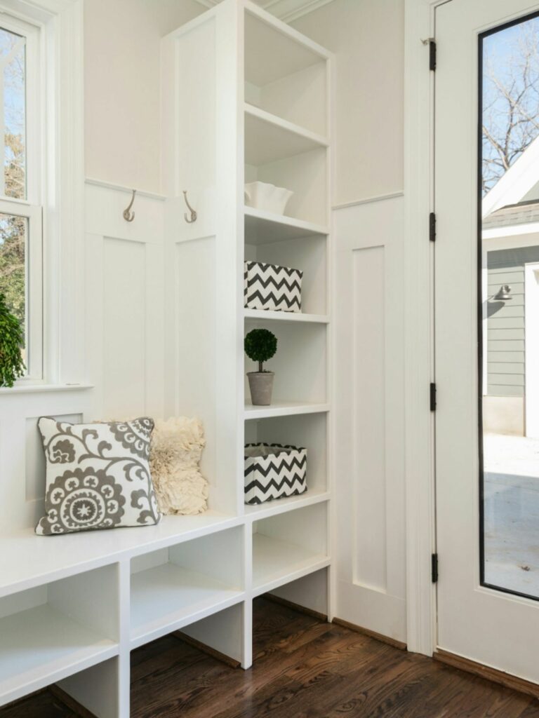 Bright mudroom entryway with built-in shelving and bench, decorative pillows, and a glass-paneled door.