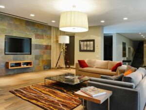 Modern living room with eclectic decor, featuring a grey sofa, colorful rug, tripod floor lamp, and mounted television.