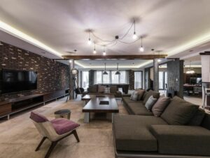 Modern living room with sectional sofa, brick accent wall, and spider-style ceiling light fixture.