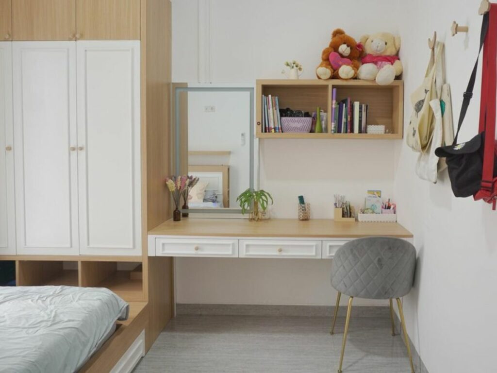 A tidy bedroom with a study area, featuring a desk, chair, bookshelves, plush toys, and mudroom organizers.