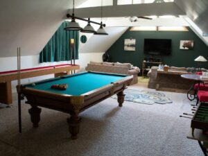 Spacious attic game room with a pool table, comfortable seating, and a television.
