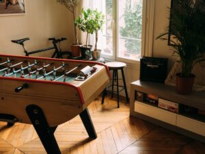 A cozy room with a foosball table, plants by the window, and a guitar amplifier.