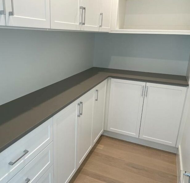 Modern laundry room corner with white cabinetry and gray countertop for organization.