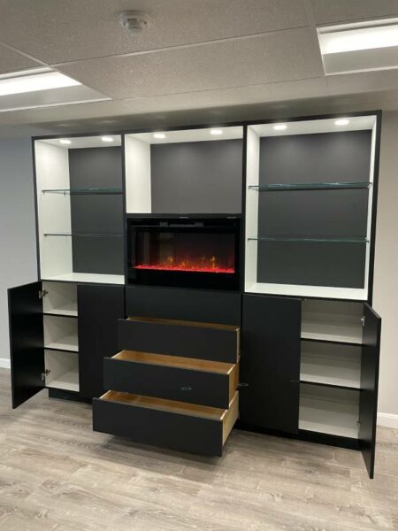 A modern black custom entertainment center with an electric fireplace and open drawers displaying storage space.