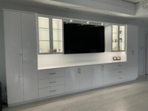 Modern living room with a wall-mounted television flanked by custom entertainment centers with white shelving and cabinetry.