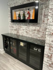 A modern black wine cabinet with glass doors and custom entertainment centers, displaying bottles against a white brick wall.