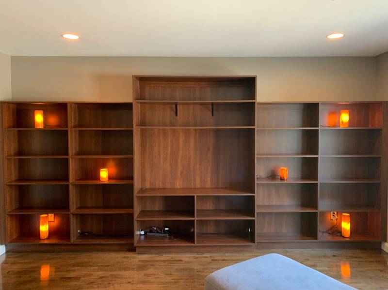 An empty wooden bookshelf with small orange lamps in a custom entertainment center in a modern room.