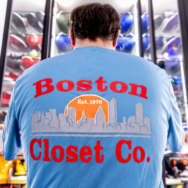 Man in a blue "Boston Closet Co." t-shirt looking at a wall display of sports helmets in a custom man cave.