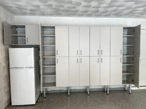A minimalist kitchen with white cabinets, a refrigerator, textured ceiling, and custom garage cabinets.