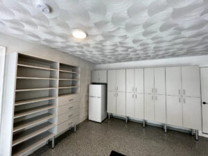 Empty modern room with textured ceiling, custom garage cabinets, and a refrigerator.