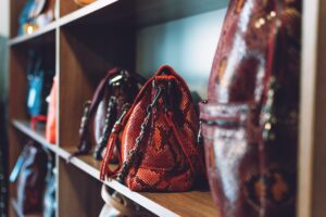 Assorted handbags displayed on wooden shelves, featuring various colors and textures, including a prominent red bag with a distinctive chain strap.