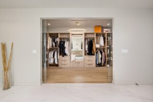 Spacious walk-in closet with wooden flooring, featuring organized shelves, hanging clothes, a central mirror, and a modern overhead light.