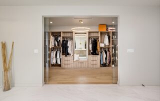 Spacious walk-in closet with wooden flooring, featuring organized shelves, hanging clothes, a central mirror, and a modern overhead light.