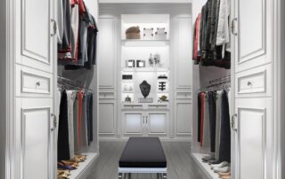A spacious walk-in closet with custom white cabinetry, clothes on hangers, folded garments, shoes on shelves, and a bench in the center showcasing how to design a custom walk in closet