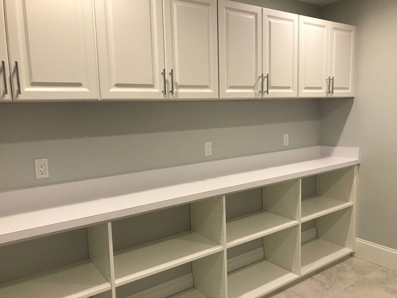 White built-in storage with upper cabinets, lower open shelves, and a countertop against a light-colored wall with multiple electrical outlets.