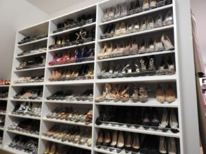 A large white shelving unit filled with many pairs of women's high-heeled shoes, arranged neatly by color and style.