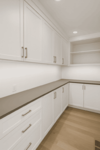 A modern pantry closet with white cabinets, drawers, open shelves, a gray countertop, and light wood flooring.