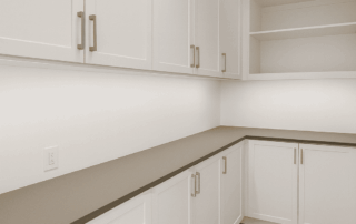 A modern pantry closet with white cabinets, drawers, open shelves, a gray countertop, and light wood flooring.