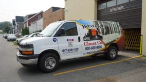 A Boston Closet Co. van is parked outside a building, featuring company branding, contact details, and social media icons on its side.