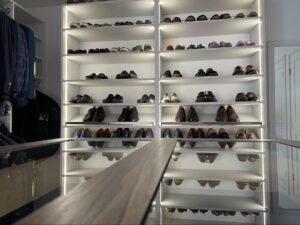 A well-lit closet with shelves neatly organized with various pairs of shoes, reflecting on a glass-topped surface in the foreground.