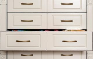 A set of six white cabinet drawers with brass handles, perfect for a reach-in closet; three are slightly open, revealing various colorful items inside.